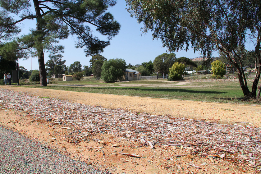 Street side view showing location of Gravel Contractors’ Encampment, modern road, footpath in the foreground, small buildings in the distance.