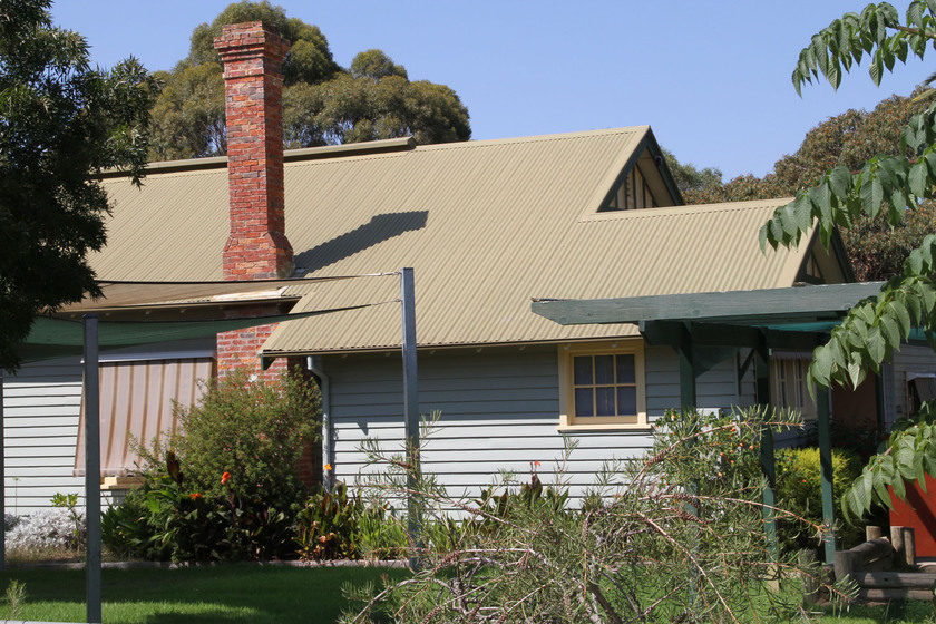 The Glenrowan School building from the side, light blue in colour, showing the weatherboard and original brick chimney.