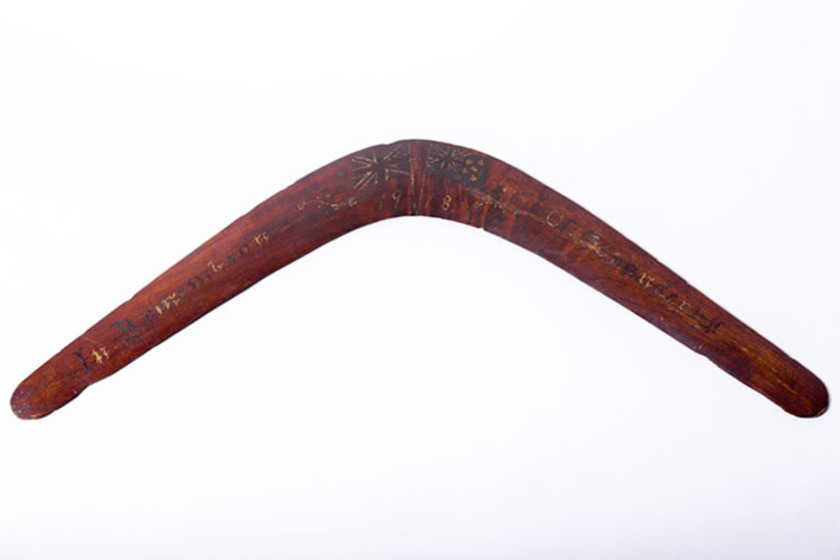 an old wooden boomerang painted with two flags at the centre point of the airfoil wings and writing across both wings