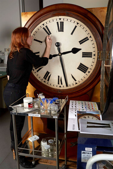 a woman cleaning a large clock face