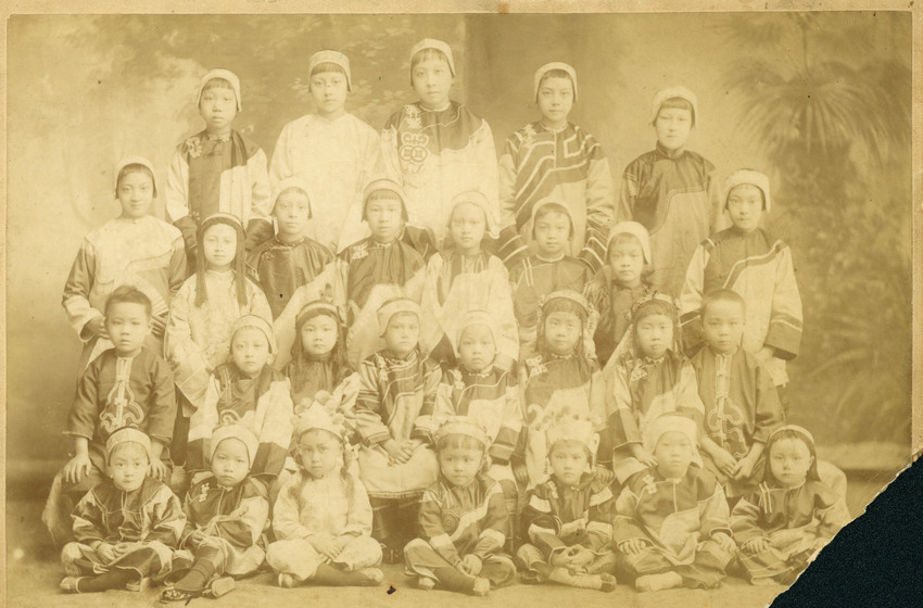 An early faded and foxing photograph of school girls in traditional Chinese dress (lined up in four rows, some standing and some sitting) 