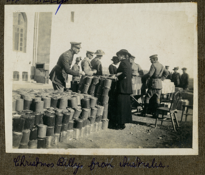Woman standing in front of billy cans, whilst serving soldiers