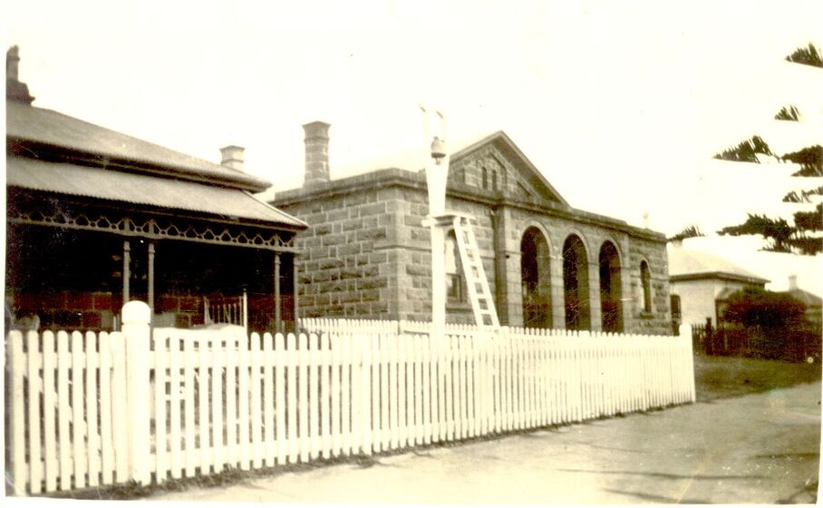 Stone house behind white picket fence with bell in foreground