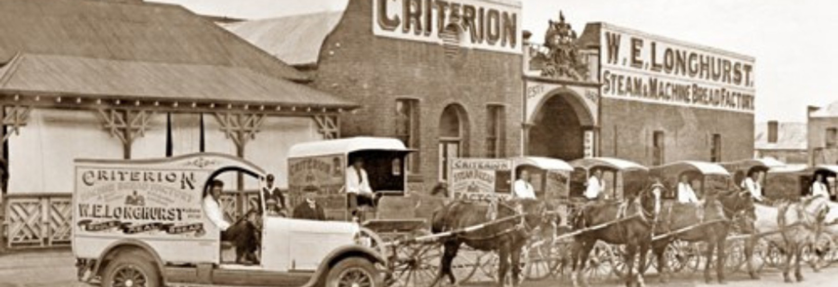 a car and several horse driven carriages in front of brick factory