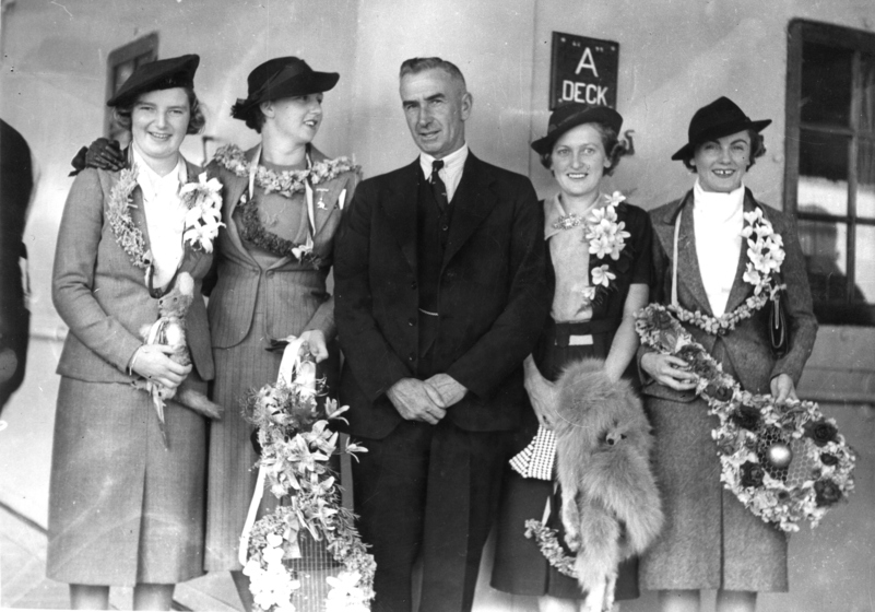 four women carry congratulatry bouquets with a suited man standing in between