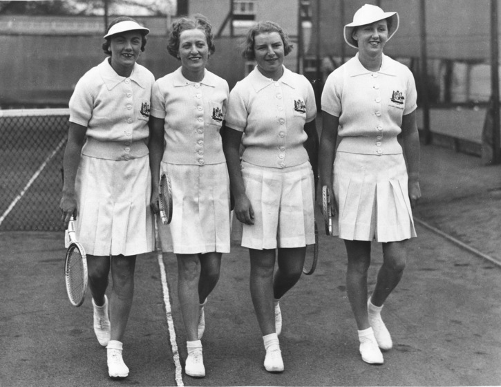 four women in tennis uniforms stand at the net