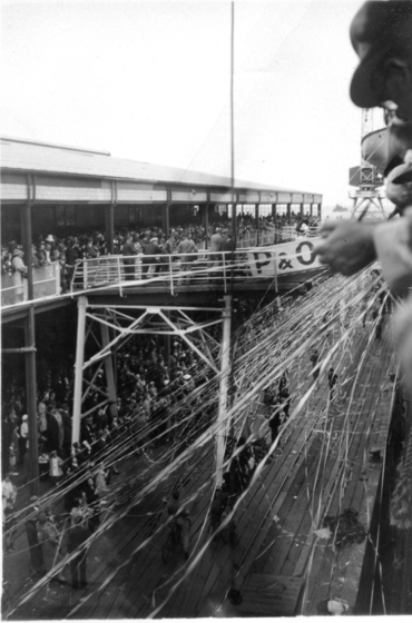 view of dock from ship's deck as passengers wave farewell