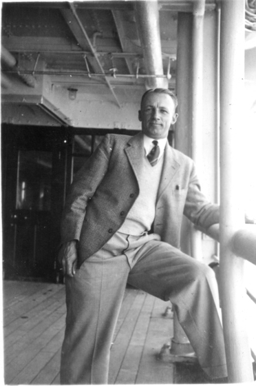 a gentleman wearing casual suit and tie leans on the side of a deck