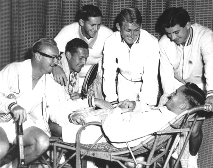 playful group of men standing over one player on a lounge, black and white