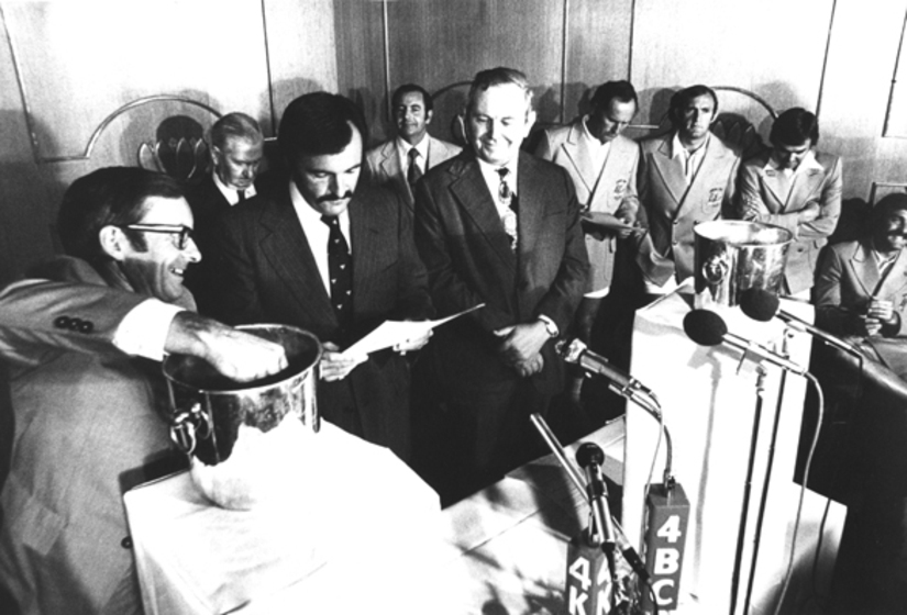 Group of men in room drawing lots from bucket