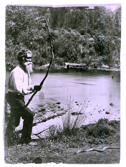 man stands beside river holding a stick above a snake