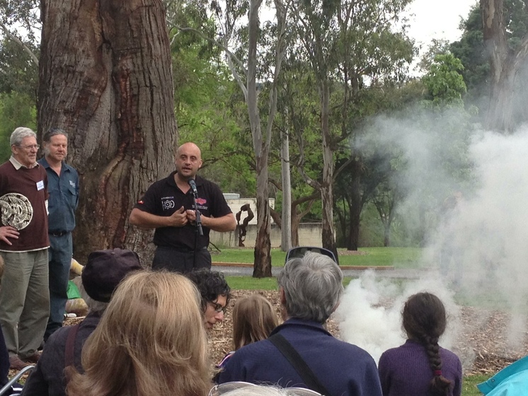 a man addresses a crowd in front of a scarred tree during a smoking ceremony