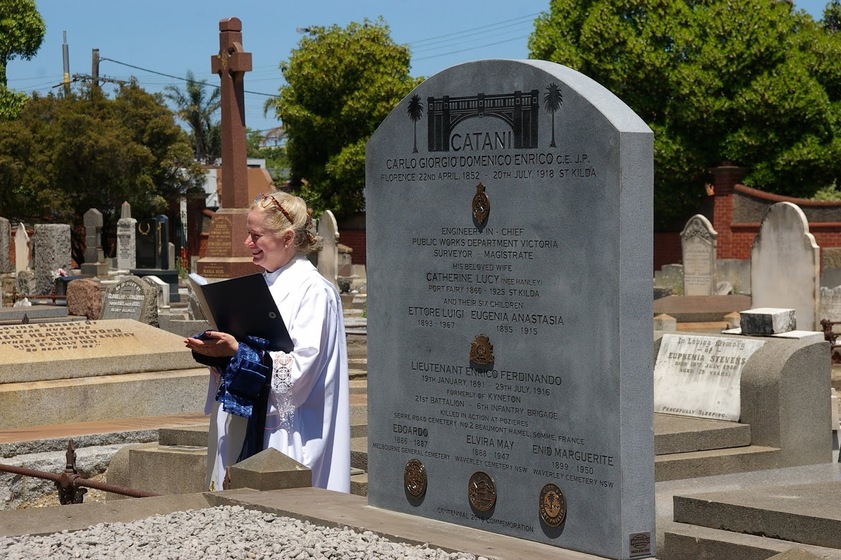 Woman standing in front of headstone, presiding over a ceremony