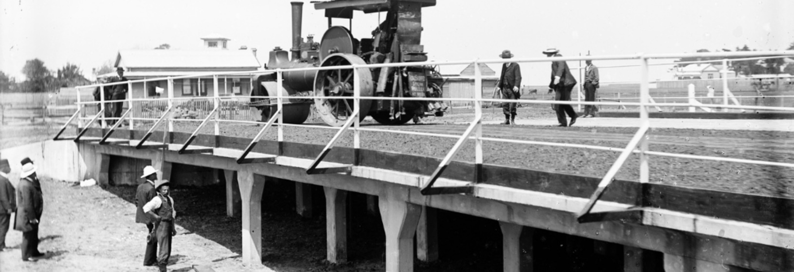 men observe a steam-driven machine crossing a bridge