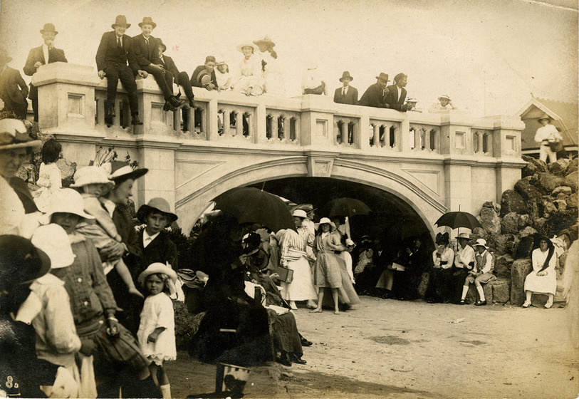 crowds gather at an archway, sitting and standing together