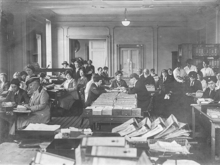 A large group of men and women in a room working on files.