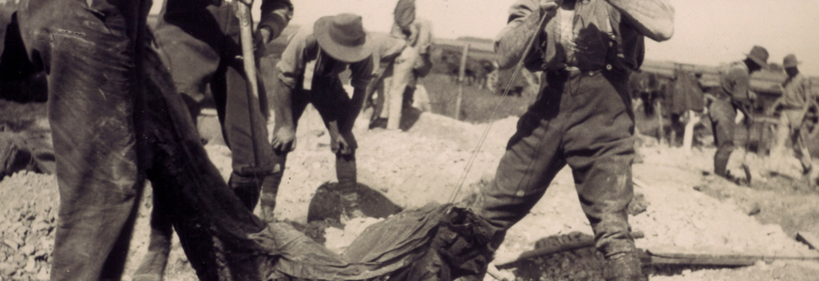 Men lifting a body wrapped in hessian out of a grave