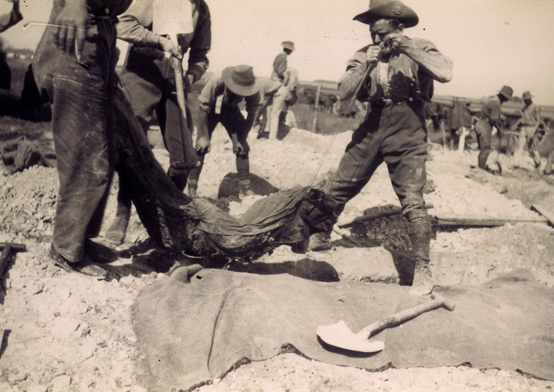Men lifting a body wrapped in hessian out of a grave.