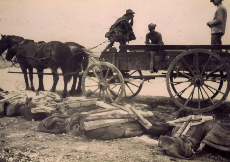 Two men sit on a horse drawn cart near hessian wrapped bodies and grave markers
