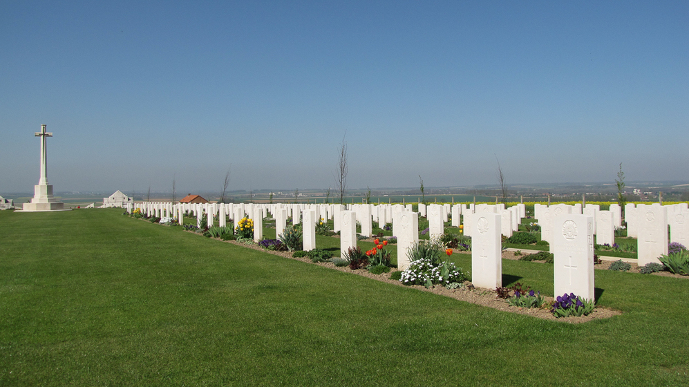 A war cemetery with stone grave markers surrounded by green fields