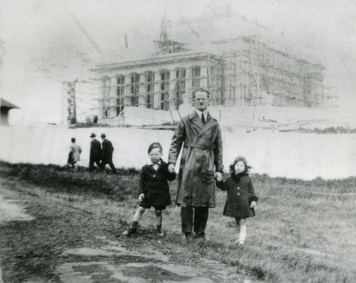 A man stands with two children in front of a partially constructed Shrine of Remembrance