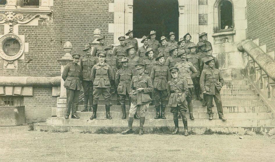 A group of men in uniform, standing on the stone steps of a brick building.