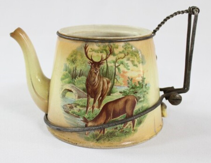 A ceramic teapot with a repaired metal handle. The teapot features a design with a woodland scene with two deer. 