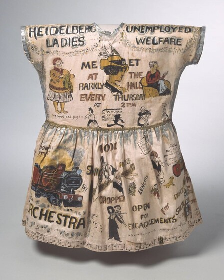 A small, cream coloured dress with figurative images and text painted on the dress in oil paint. 