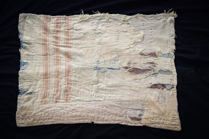 A hand stitched white and blue cot quilt made from scrap fabric.