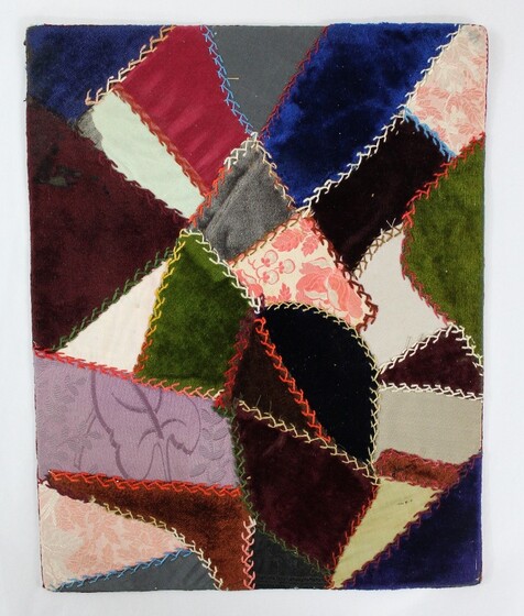 A quilt sampler featuring multi-coloured fabric of different textures, hand stitched and mounted on cardboard. 