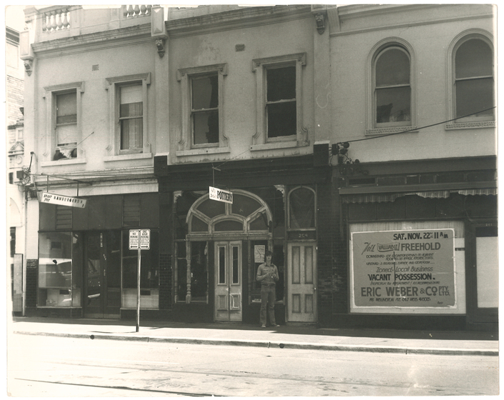 Man standing outside two-storey Victorian shopfront.