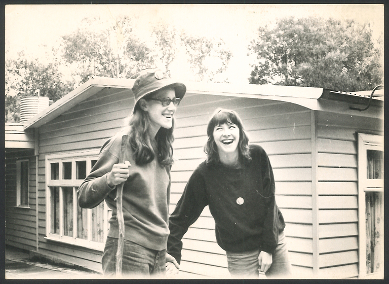 Two women laughing outside a weatherboard house.