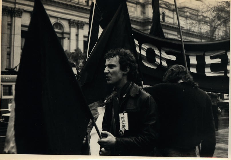 Black and white photograph of a demonstrator on a street holding a flag and with a label on his coat 'PUFTER'.