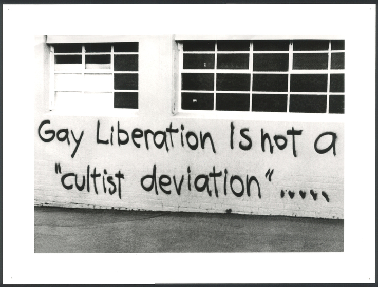 Black and white photograph of graffiti spray painted on a wall.