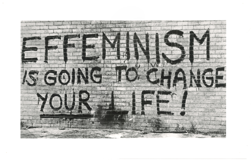 Black and white photograph of graffiti spray painted on a brick wall.