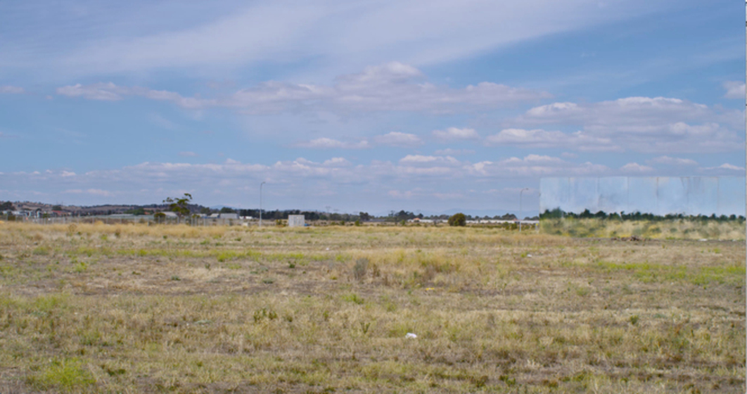 Still of video depicting large open grass field and sky with building in distance painted with grass and sky, to blend into the landscape. 