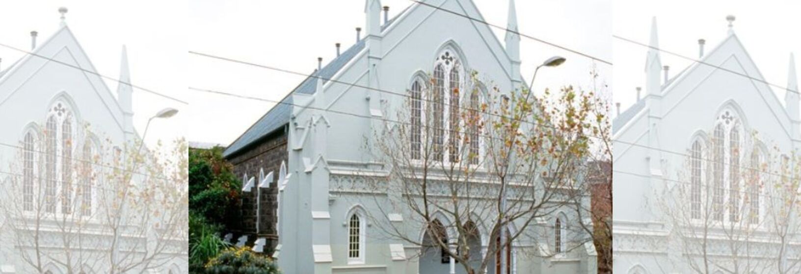 Buiding facade of pitch roofed, pale blue, brick church with three-arch entry and upper stained glass windows.