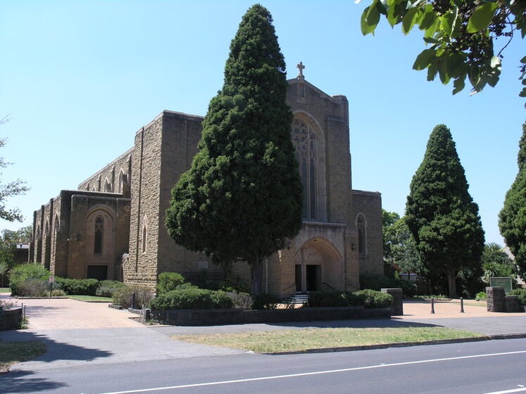 Large sandstone bricked building centre with tall green leafed tree in the foreground