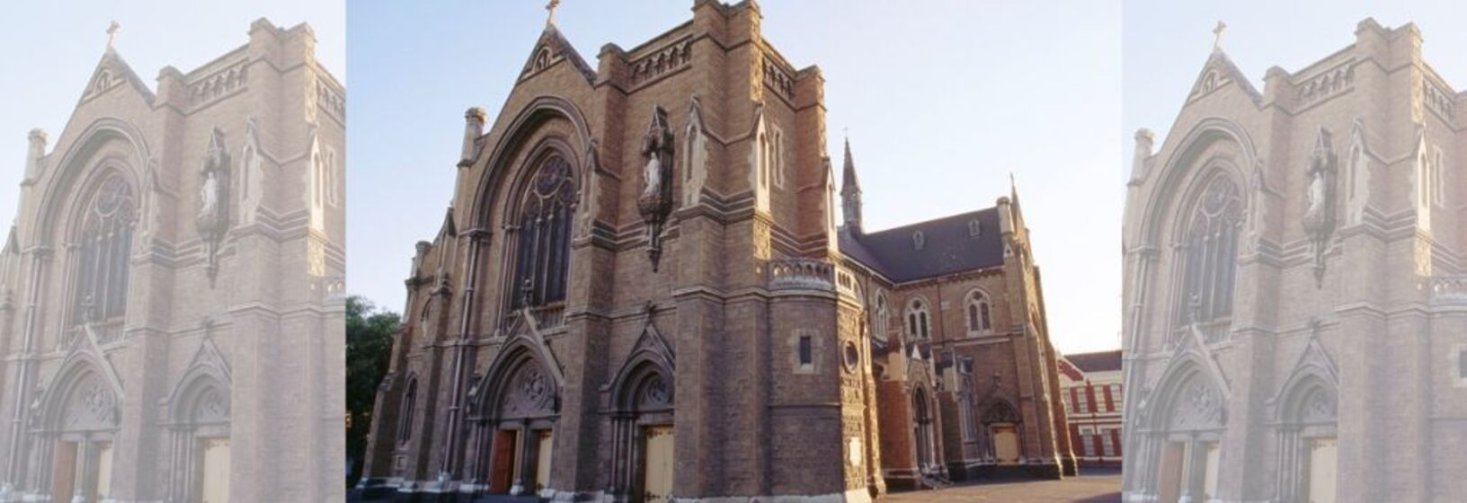Large neo-gothic sandstone church with arched stain glass windows and wooden doors inserted into the facade