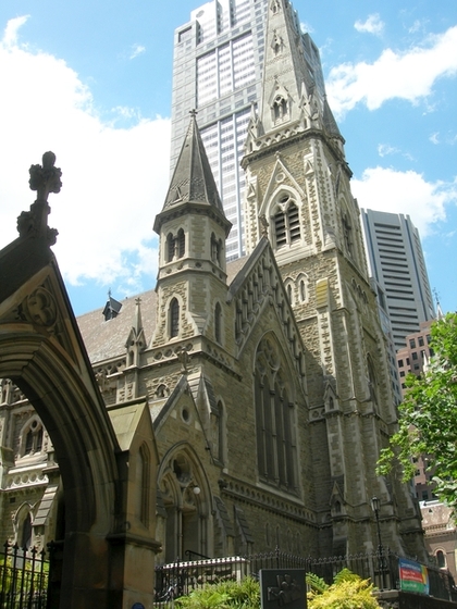 Large church with two steeples out the front, one much taller than the other. Tall office building stands behind the church