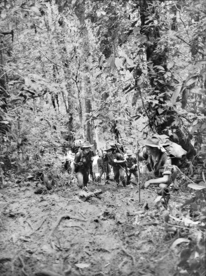 Black and white photograph of small group of soldiers struggling to proceed on very muddy track in the jungle.