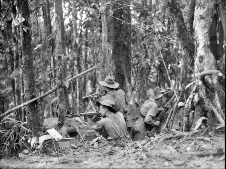 Black and white photograph of three soldiers in hole in ground firing rifles into the jungle.