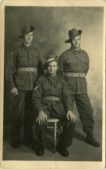 Black and white studio photograph of two Australian soldiers standing and one sitting in front.