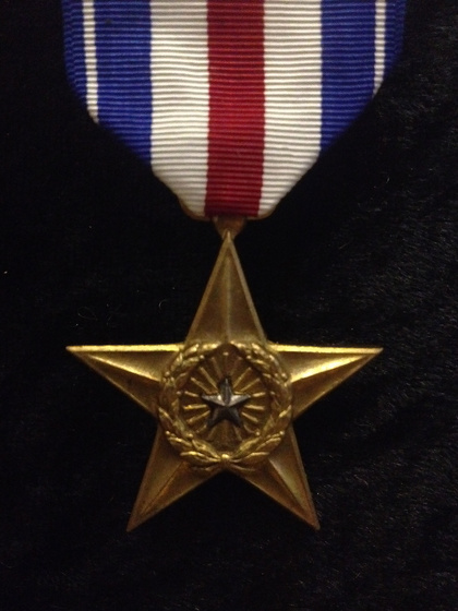 Gold star-shaped medal with a wreath in the centre hanging on a red, white and blue ribbon.