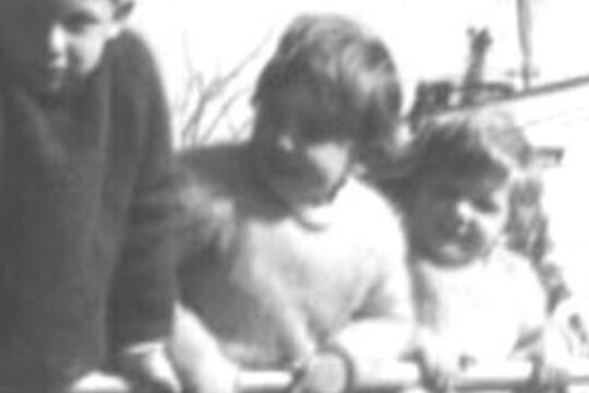 Black and white image of three small children leaning on what appears to be a large iron fence
