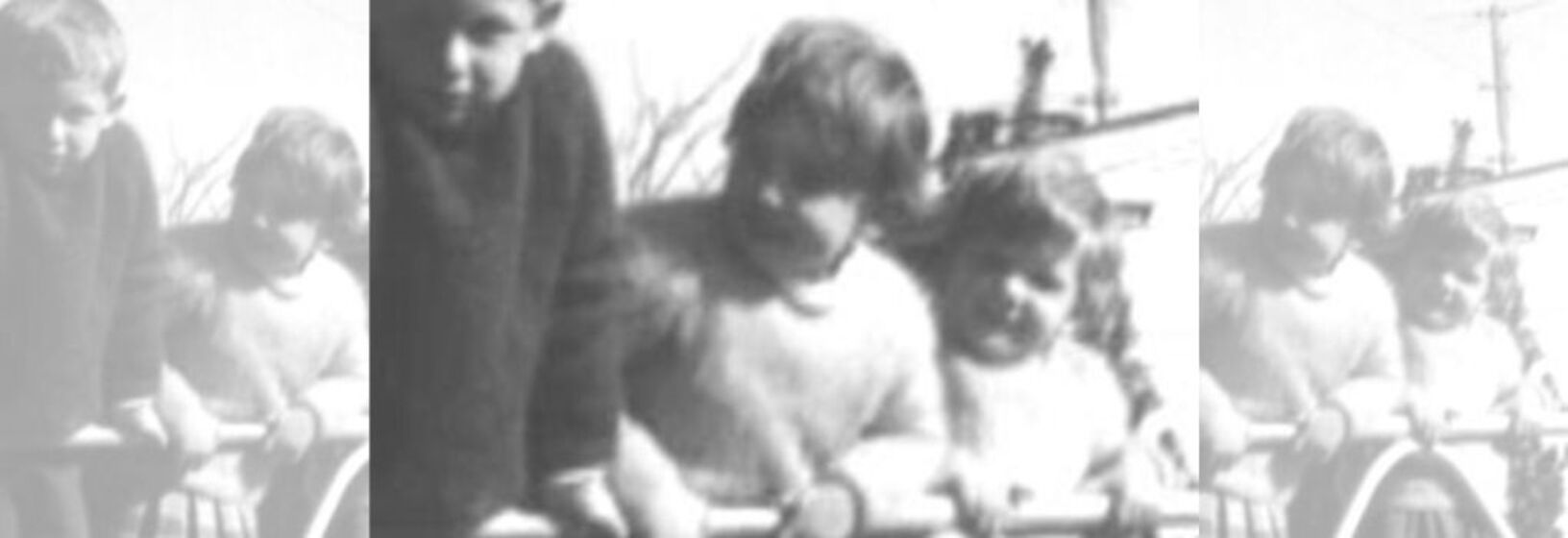 Black and white image of three small children leaning on what appears to be a large iron fence