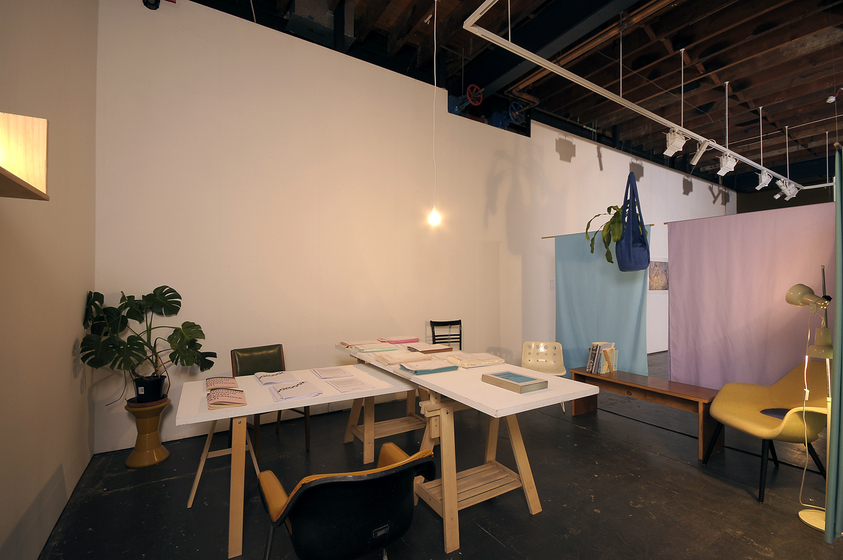 Installation of chairs, plants and a desk with objects on it.