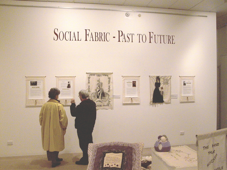 Colour photograph of gallery interior with two patrons viewing visual art on the wall.