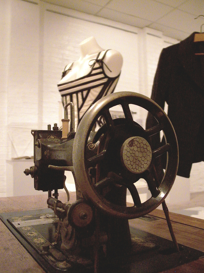 Colour photograph of gallery interior with Victorian sewing machine in foreground and mannequin in background.