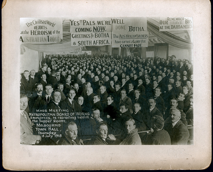 Black and white photograph of large gathering of men seated under banners.